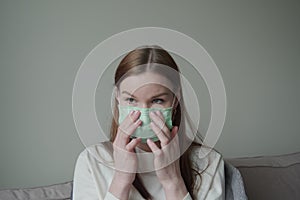 A beautiful young girl with red hair is afraid to get coronovirus and put on a green medical mask on her face. Orvi, coronovirus. photo