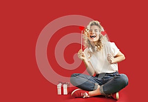 Beautiful young girl with red hearts and a white gift with a bow sits in full growth on an isolated red backgroundValentine`s Day