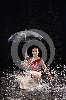 Beautiful young girl in red sportswear with umbrella in aqua studio. Drops of water spread about her fitness body. The