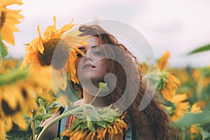Beautiful young girl with red wavy hair and freckles in stripped colourful dress enjoying nature on the field of sunflowers.