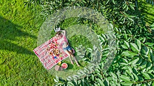 Beautiful young girl relaxing on grass, having summer picnic in park outdoors, aerial view from above