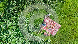 Beautiful young girl relaxing on grass, having summer picnic in park outdoors, aerial view from above