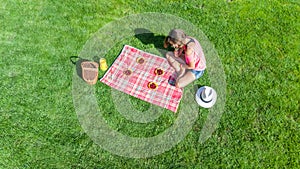 Beautiful young girl relaxing on grass, having summer picnic in park outdoors, aerial view from above