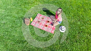 Beautiful young girl relaxing on grass, having summer picnic in park outdoors, aerial view from above