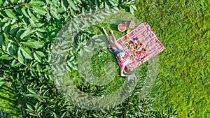 Beautiful young girl relaxing on grass, having summer picnic in park outdoors, aerial view from above