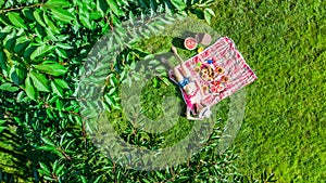 Beautiful young girl relaxing on grass, having summer picnic in park outdoors, aerial view from above