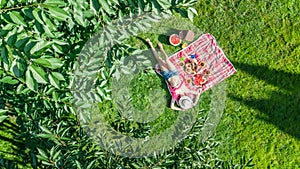 Beautiful young girl relaxing on grass, having summer picnic in park outdoors, aerial view from above