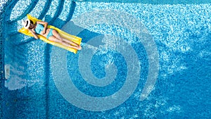 Beautiful young girl relaxing in swimming pool, swims on inflatable mattress and has fun in water on family vacation