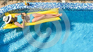 Beautiful young girl relaxing in swimming pool, swims on inflatable mattress and has fun in water on family vacation