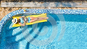 Beautiful young girl relaxing in swimming pool, swims on inflatable mattress and has fun in water on family vacation