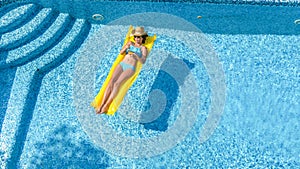 Beautiful young girl relaxing in swimming pool, swims on inflatable mattress and has fun in water on family vacation