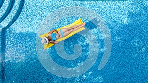 Beautiful young girl relaxing in swimming pool, swims on inflatable mattress and has fun in water on family vacation, aerial view