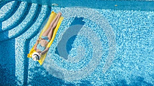 Beautiful young girl relaxing in swimming pool, swims on inflatable mattress and has fun in water on family vacation, aerial view