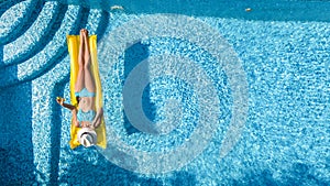 Beautiful young girl relaxing in swimming pool, swims on inflatable mattress and has fun in water on family vacation, aerial view