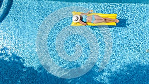 Beautiful young girl relaxing in swimming pool, swims on inflatable mattress and has fun in water on family vacation, aerial view