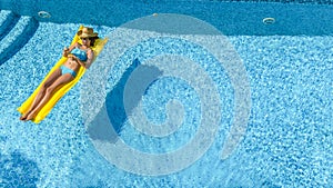 Beautiful young girl relaxing in swimming pool, swims on inflatable mattress and has fun in water on family vacation, aerial view