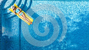 Beautiful young girl relaxing in swimming pool, swims on inflatable mattress and has fun in water on family vacation, aerial view