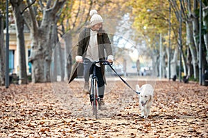 Beautiful young girl riding a bike while walking her dog in the park in autumn