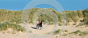 Beautiful young girl riding a Friesian mare on the coast of Hauts-de-France