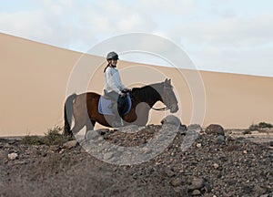 Beautiful young girl riding a horse in the desert of the Canary Islands.