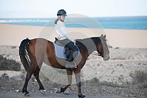 Beautiful young girl riding a horse in the desert of the Canary Islands.