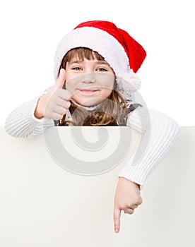 Beautiful young girl with santa hat standing behind white board.