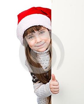 Beautiful young girl with santa hat standing behind white board on white