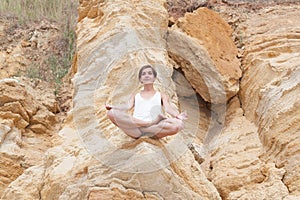 A beautiful young girl with short hair is dressed in shorts and a white jersey is practicing yoga on the background of rocks.