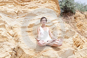 A beautiful young girl with short hair is dressed in shorts and a white jersey is practicing yoga on the background of rocks. Pose