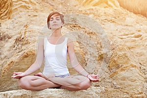 A beautiful young girl with short hair is dressed in shorts and a white jersey is practicing yoga on the background of rocks. Pose