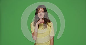 Beautiful young girl show silence gesture ask to be quiet, keep secret on chromakey green background. Privacy concept