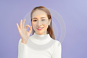 Beautiful young girl showing OK sign against violet background