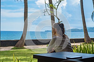 Beautiful young girl sits on the veranda the bungalow looks into the distance on the ocean beach in Bali island Indonesia