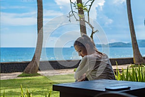 Beautiful young girl sits and waiting for a phone call on the veranda the bungalow on the ocean beach in Bali island Indonesia