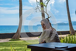 Beautiful young girl sits and waiting for a phone call on the veranda the bungalow on the ocean beach in Bali island Indonesia