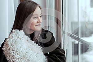 Beautiful young girl sitting alone on the windowsill and looking out the window