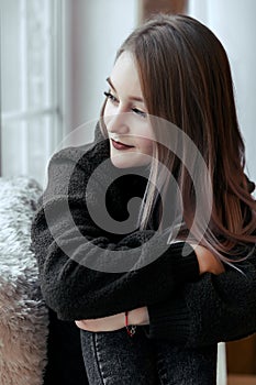 Beautiful young girl sitting alone on the windowsill and looking out the window