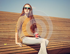 Beautiful young girl sitting on a bench on a warm summer day whis cuo of coffee