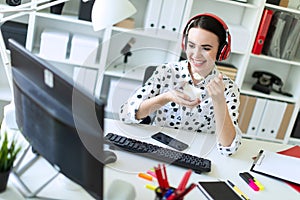 Beautiful young girl sitting in headphones at desk in office, eating yogurt and looking at monitor.