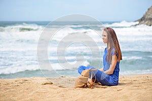 Beautiful young girl sitting with her bag on the beach on vacation