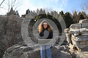 Beautiful young girl sitting with a laptop in the park on a background of mountains. The possibilities are endless on the Internet