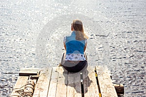A beautiful and young girl is sitting on a pier