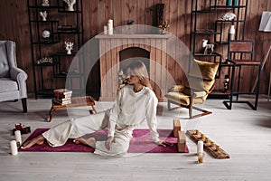 Beautiful young girl sitting relaxing on mat with candles in stylish cozy comfort home interior with comfy furniture