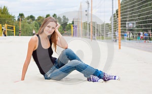 Beautiful young girl sitting on the sand nex to the net for volleyball of Sunny warm day