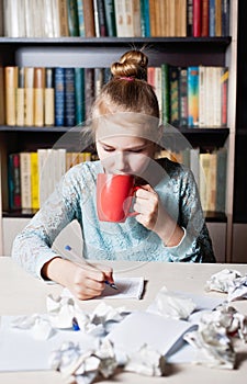 Beautiful young girl sitting on workplace with crumpling the sheet.