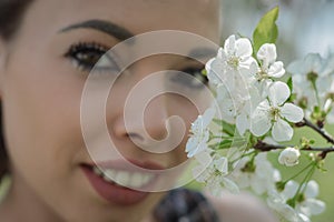 Beautiful young girl smelling a twig of blooming cherry flowers in a sunny spring day.