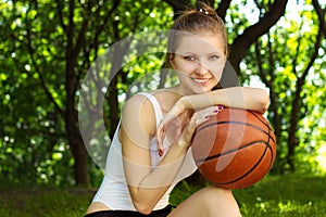 Beautiful young girl with a smile, sitting with a basketball ball in for sports