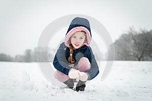 Beautiful young girl smiling happy playing outside in falling snow looking at camera wrapped up warm with blue coat hood up gloves