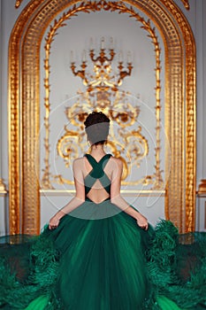 Ð beautiful young girl standing in a haute couture green dress in a luxurious gold interior.