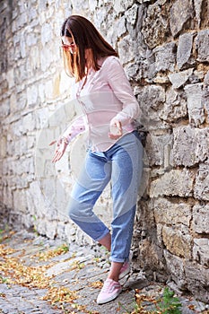 Beautiful young girl standing near the stone wall. Portrait pretty young fashion girl near a stone wall. Beautiful blonde woman